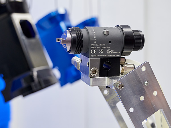 A Stellair Auto automatic air spray gun at the end of a robot arm points and sprays paint on a part.